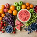Assortment of fresh whole fruits including apples, berries, and watermelon on a wooden table, representing healthy fruit choices for weight loss